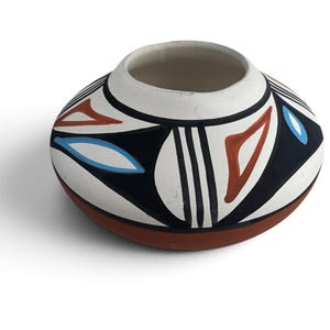May include: A low-profile, rounded ceramic pot with a wide opening. The exterior features a matte white upper section decorated with bold black geometric lines, terracotta-colored triangles, and light blue leaf-shaped accents over a terracotta base.