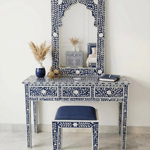 May include: A navy blue vanity set with a matching mirror, stool, and decorative accents. The set features intricate white floral and star patterns. The mirror has an arched top. A blue notebook and vase are on the vanity.