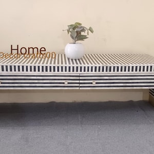 May include: A long, low coffee table with a black and white striped bone inlay top. The table has two drawers and gold metal legs.