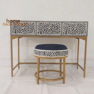 May include: A black and white bone inlay desk with three drawers and a gold metal frame. The desk is paired with a matching stool with a blue velvet cushion.