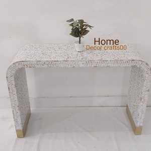 May include: White console table with a curved design and a mother of pearl inlay. The table has a gold base and is decorated with a leaf pattern. Home Decor crafts00 is written on the table.