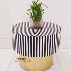 May include: Black and white striped round side table with a gold base. A small potted plant sits on top of the table.