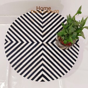 May include: A round, black and white striped side table made of bone inlay. The table has a geometric pattern and is topped with a small potted plant.