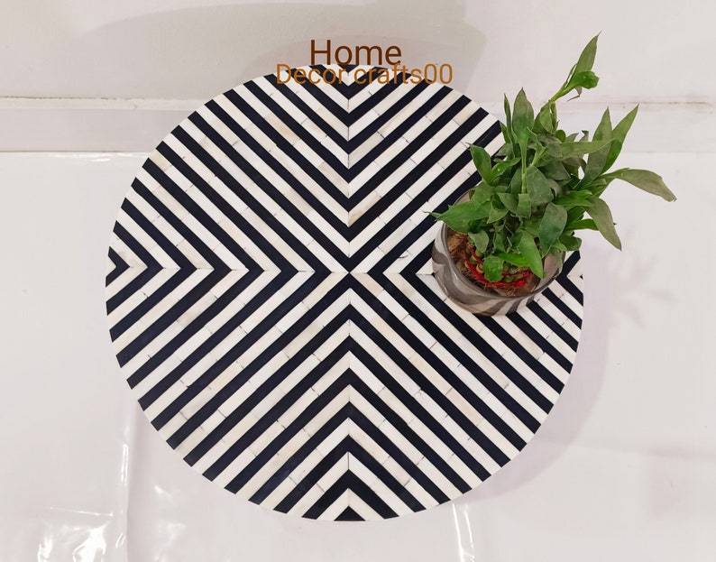 May include: A round, black and white striped side table made of bone inlay. The table has a geometric pattern and is topped with a small potted plant.