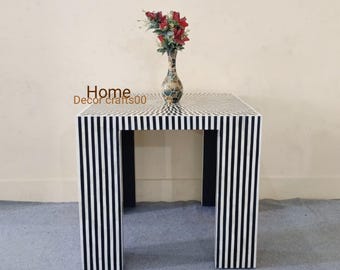 Pode incluir: Mesa de apoio de listras pretas e brancas feita de incrustações de osso. A mesa tem um tampo quadrado e quatro pernas. Um vaso com flores vermelhas está em cima da mesa.