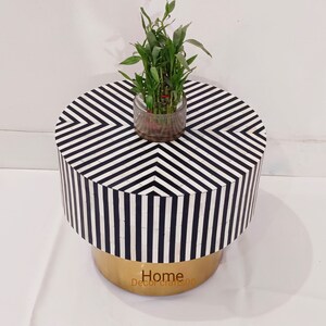 May include: A round black and white striped side table with a gold base. A small potted plant sits on top of the table.