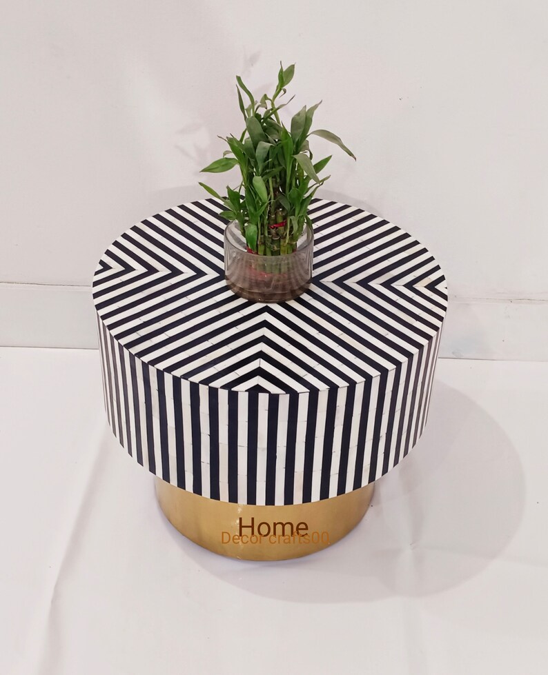 May include: A round black and white striped side table with a gold base. A small potted plant sits on top of the table.