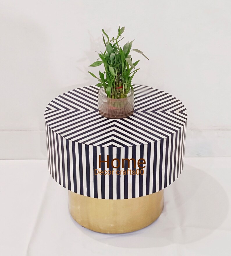 May include: Black and white striped round side table with a gold base. A small potted plant sits on top of the table.