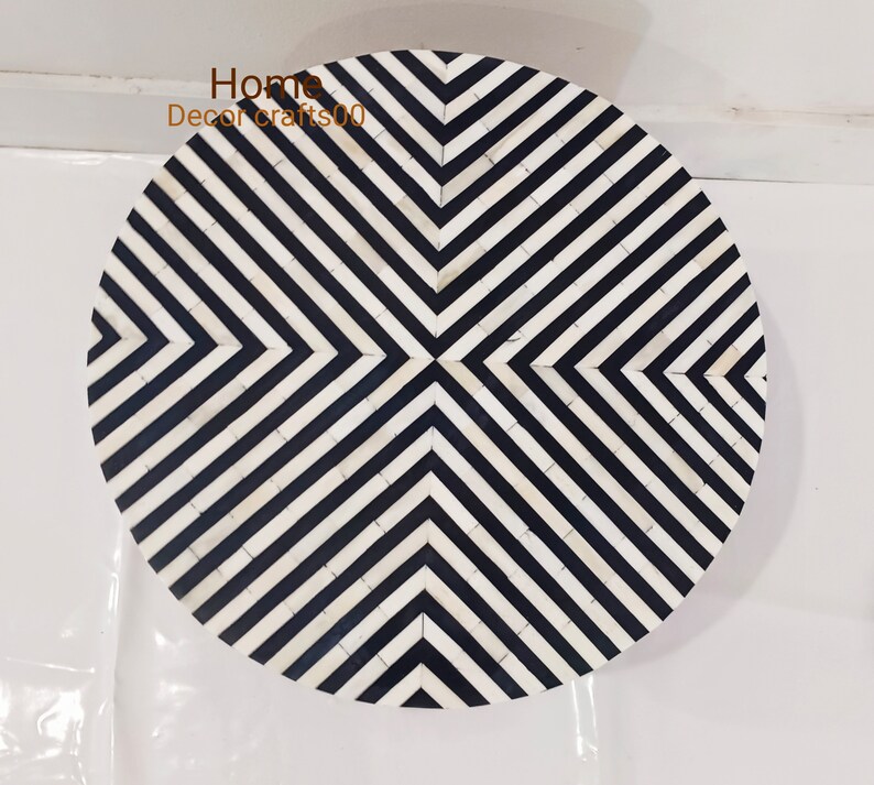 May include: Round black and white bone inlay table top with a geometric pattern. The pattern is made up of black and white stripes that form a diamond shape in the center.