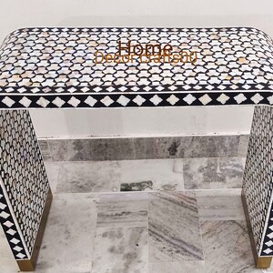 May include: A black and white console table with a geometric pattern made of mother of pearl inlay. The table has a curved design and a gold base.