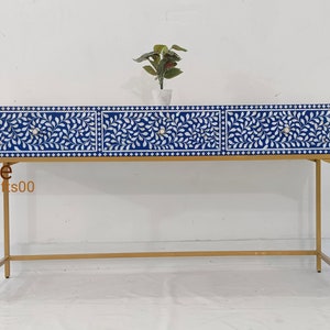 May include: A blue and white console table with three drawers and a gold metal frame. The drawers have a floral pattern and are made of bone inlay. The table is 48 inches long and 18 inches wide.