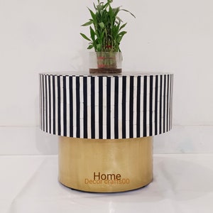 May include: A round, black and white striped side table with a gold base. The table is made of bone inlay and has a plant on top of it. The text "Home Decor crafts00" is on the base of the table.