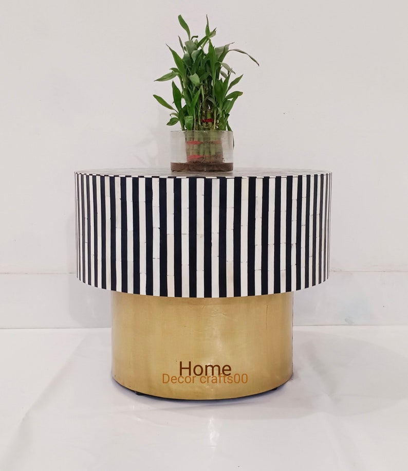 May include: A round, black and white striped side table with a gold base. The table is made of bone inlay and has a plant on top of it. The text "Home Decor crafts00" is on the base of the table.
