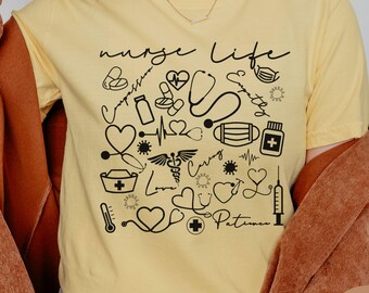 May include: Butter yellow t-shirt with the words "nurse life" in a handwritten font, along with various medical-themed illustrations in black. The illustrations include hearts, stethoscopes, and medical symbols. The shirt is a crew neck.