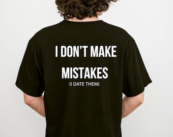 May include: A black short-sleeved t-shirt featuring white text on the back that reads I DON'T MAKE MISTAKES (I DATE THEM) in a clean, sans-serif font. The shirt has a standard crew neckline and a simple, solid-colored design.