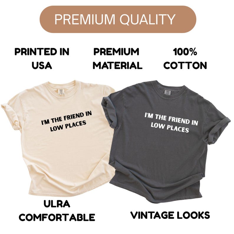 May include: Two t-shirts, one cream-colored and one charcoal gray, are displayed. Both shirts have the text "I'M THE FRIEND IN LOW PLACES" printed in white. The cream shirt has the words "ULRA COMFORTABLE" printed below the text, and the gray shirt has "VINTAGE LOOKS".