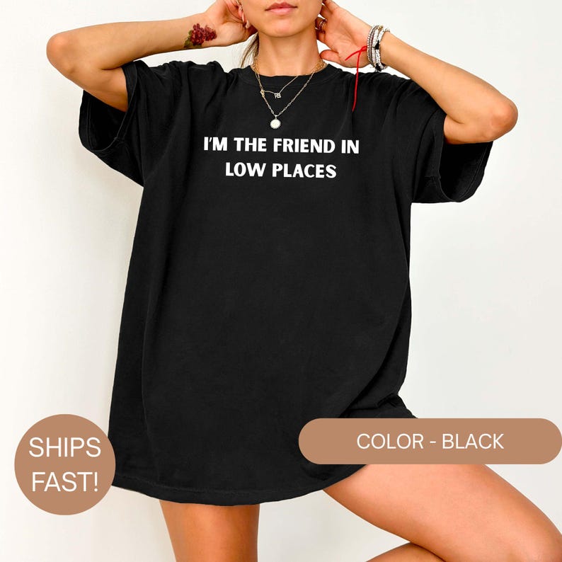 Model wearing a black Comfort Colors oversized t-shirt with white text reading “I’m the Friend in Low Places,” relaxed casual fit