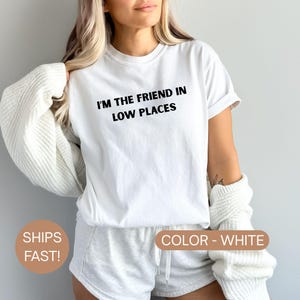 Model wearing a white Comfort Colors oversized t-shirt with white text reading “I’m the Friend in Low Places,” relaxed casual fit