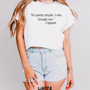 May include: White t-shirt with the quote "It's pretty simple. I win. Google me." and the name "-Cignetti". The text "WHITE SANGCUSTOMTEE" is printed at the bottom. The shirt is paired with light blue denim shorts.