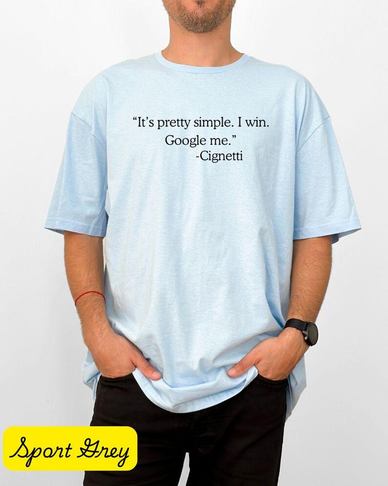 May include: Light blue t-shirt with the quote "It's pretty simple. I win. Google me." attributed to Cignetti in black text. The shirt is worn by a person with their hands in their pockets. The words "Sport Grey" are in a yellow rectangle.