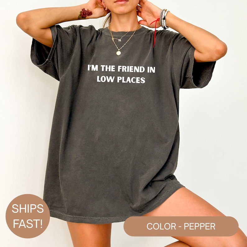 Model wearing a pepper Comfort Colors oversized t-shirt with white text reading “I’m the Friend in Low Places,” relaxed casual fit