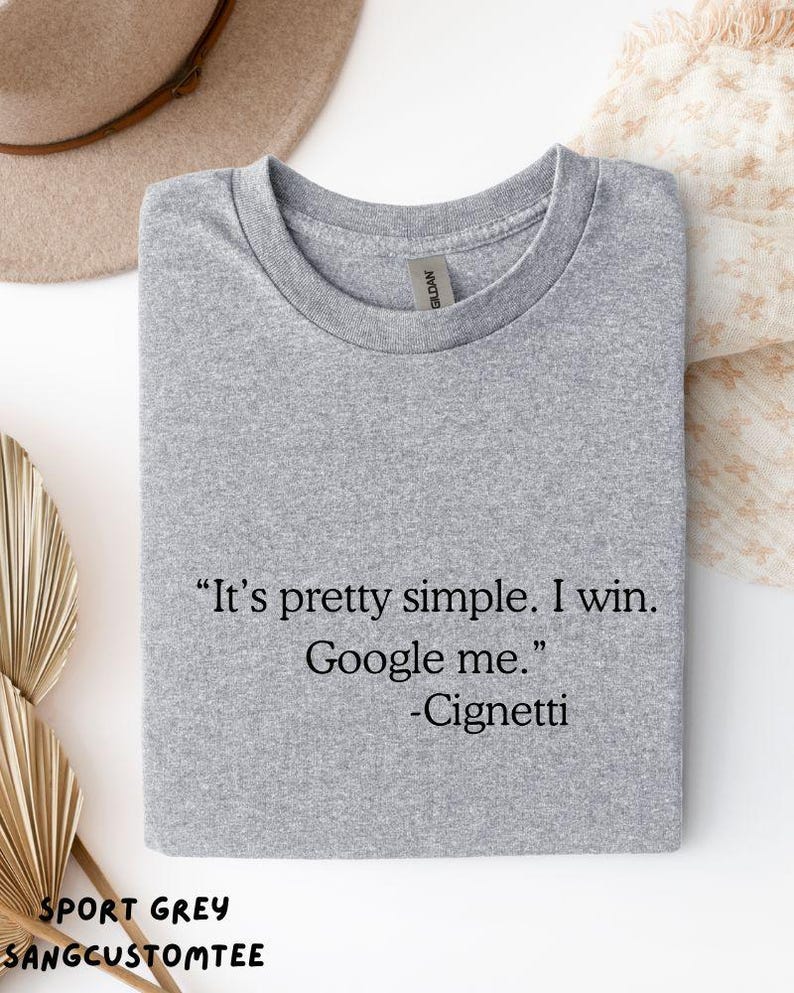 May include: Sport grey t-shirt with the text "It's pretty simple. I win. Google me." and the name "-Cignetti" in black. The shirt is folded and has a Gildan tag.