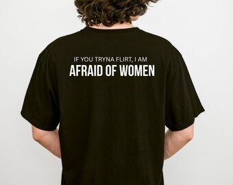May include: A black short-sleeved t-shirt featuring white text on the back that reads IF YOU TRYNA FLIRT, I AM AFRAID OF WOMEN. The shirt has a crew neckline and a standard fit, displayed from the back view to show the printed message clearly.