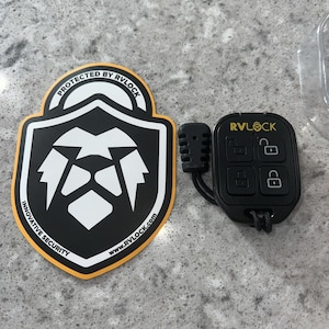 May include: Black RVLOCK key fob with four buttons and the RVLOCK logo in yellow. A black and white sticker with the text "PROTECTED BY RVLOCK" and "INNOVATIVE SECURITY" is also in the image.