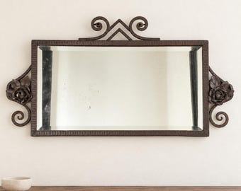 May include: A rectangular wall mirror featuring a dark brown metal frame with a textured finish. The frame is adorned with decorative scrollwork at the top and sides, with sculpted rose flower motifs integrated into the side scroll elements.