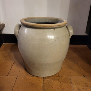 Puede incluir: Una gran olla de cerámica blanca con dos asas. La olla tiene una forma ligeramente redondeada y está decorada con líneas horizontales.