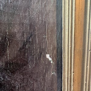 Op de afbeelding: Close-up van een deel van een houten frame. De linkerkant is een donkerbruin, verweerd hout met witte strepen. De rechterkant is een lichtbruin, geribbeld hout met verticale lijnen.