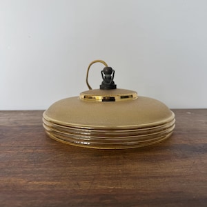May include: A gold and brown glass pendant light fixture with a textured glass shade and a gold rim. The light fixture has a simple design with a single bulb.