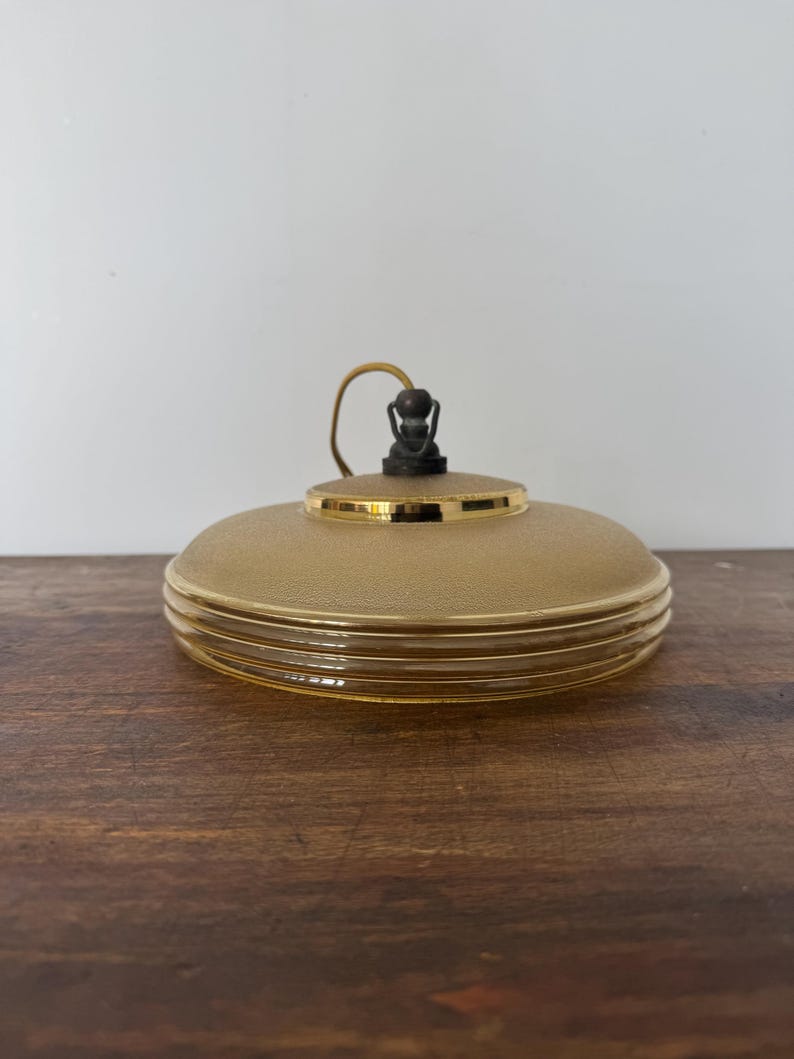 May include: A gold and brown glass pendant light fixture with a textured glass shade and a gold rim. The light fixture has a simple design with a single bulb.