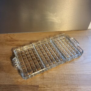 Puede incluir: Una bandeja de servir de vidrio transparente con tres secciones divididas. La bandeja tiene un patrón texturizado en relieve y es perfecta para servir aperitivos o entremeses.