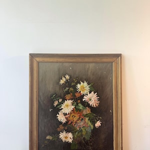 Op de afbeelding: Een antiek, ingelijst bloemenschilderij. Het kunstwerk toont een boeket witte, gele en oranje bloemen tegen een donkere achtergrond. De houten lijst heeft een warme, gouden tint, wat de vintage uitstraling versterkt.