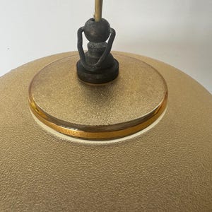 May include: A gold-colored glass pendant light fixture with a textured surface and a gold trim. The fixture has a simple, round shape and a metal hook for hanging.