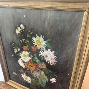 Op de afbeelding: Olieverfschilderij van een boeket bloemen in een goudkleurige houten lijst. De bloemen zijn wit, roze en oranje, met groene bladeren tegen een donkergrijze achtergrond. De lijst heeft een getextureerd oppervlak.