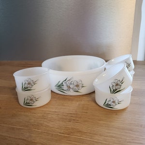 Puede incluir: Un juego de seis cuencos de cerámica blanca con un diseño floral. Los cuencos son de varios tamaños, con el cuenco más grande en el centro y cinco cuencos más pequeños que lo rodean. Los cuencos están decorados con una flor blanca y hojas verdes.