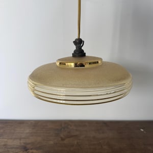 May include: A gold and white glass pendant light with a textured surface and a gold rim. The light has a simple design with a round shape and a single bulb.