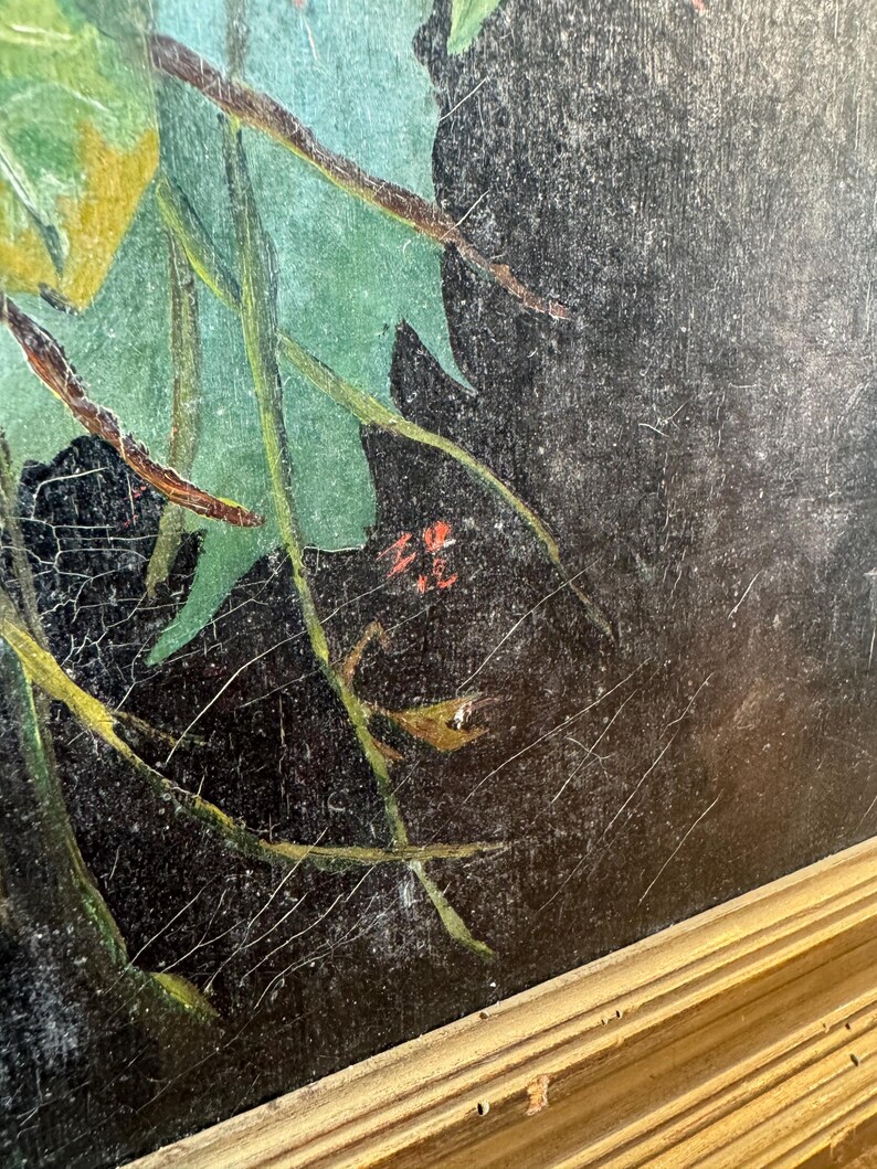 Op de afbeelding: Een antiek schilderij met een gouden lijst. Het kunstwerk toont een donkere achtergrond met groene bladeren en takken. Het schilderij vertoont zichtbare scheuren en slijtage, wat bijdraagt aan de vintage charme. De handtekening van de kunstenaar is zichtbaar in het midden onderaan.