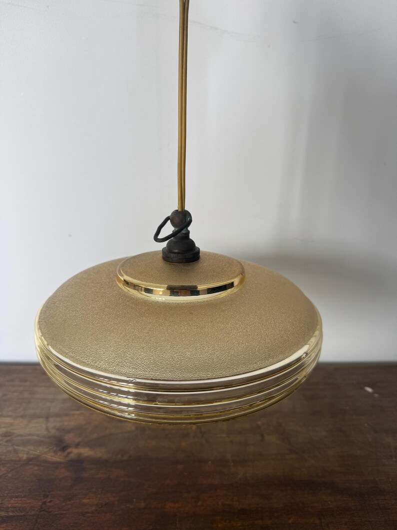 May include: A gold-colored pendant light with a round, textured glass shade. The shade has three horizontal lines around the bottom.