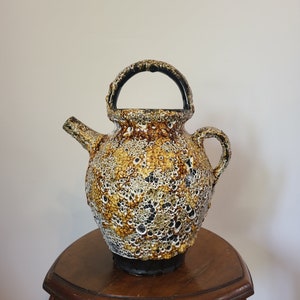 May include: A brown and white ceramic pitcher with a textured surface and a black handle. The pitcher is sitting on a wooden table.
