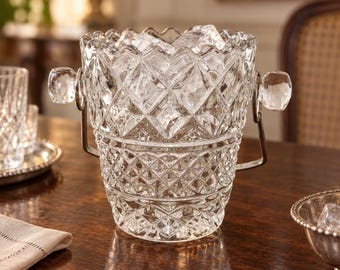 May include: A clear glass ice bucket featuring a diamond-cut pattern, a scalloped top rim, and a silver-toned metal swing handle with glass side accents. The bucket is filled with several clear ice cubes, showcasing its reflective texture.