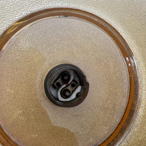 May include: Close-up of a light bulb socket inside a clear glass lampshade with a gold rim.