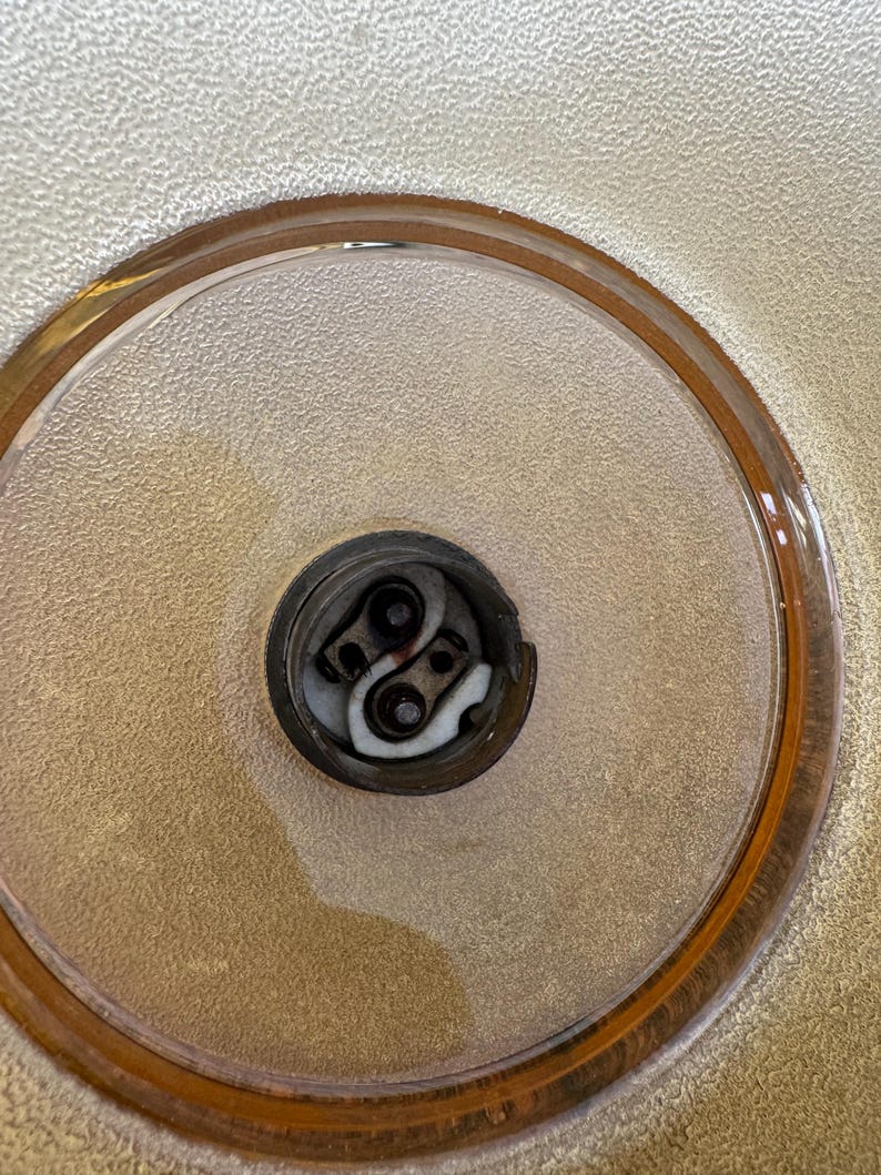 May include: Close-up of a light bulb socket inside a clear glass lampshade with a gold rim.