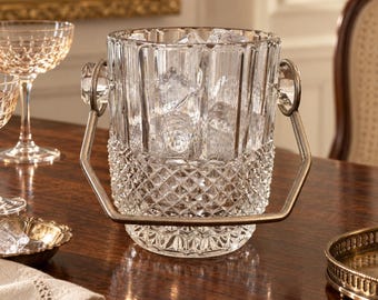 May include: A clear glass ice bucket featuring a vertical ribbed upper section and a diamond-cut textured base. The bucket includes a metallic handle attached to two side rings and is filled with several clear ice cubes for cooling purposes.