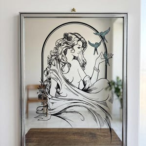 May include: A rectangular wall mirror with a silver frame featuring a black line art illustration of a person with long flowing hair and flowers, positioned within an arched border, interacting with three small birds flying near their hand.