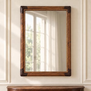 May include: A rectangular wall mirror featuring a medium-brown wooden frame with a visible grain texture. The four corners of the frame are accented with dark brown, ribbed, wrap-around corner details that provide a distinct contrast.