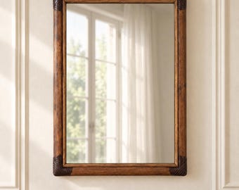 May include: A rectangular wall mirror featuring a medium-brown wooden frame with a visible grain texture. The four corners of the frame are accented with dark brown, ribbed, wrap-around corner details that provide a distinct contrast.
