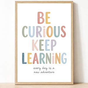 May include: A framed wall art print featuring the text BE CURIOUS KEEP LEARNING in large, multi-colored, rounded letters, followed by the smaller text every day is a new adventure in a simple black font, all set against a plain white background.